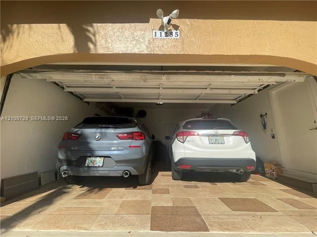 Two-car garage featuring a sectional overhead door, tile flooring, and integrated exterior security lighting
