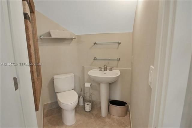 Powder room featuring a white pedestal sink with a chrome faucet, a dual-flush toilet, stone-finish tile flooring, and wall-mounted metal hardware