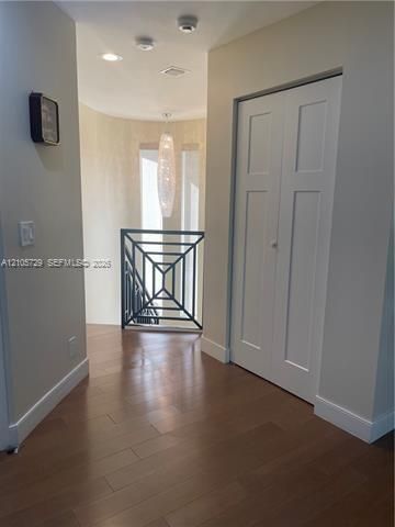 Interior hallway featuring wood-finish flooring, a geometric-patterned metal railing, a tiered hanging pendant light, and a white bifold closet door
