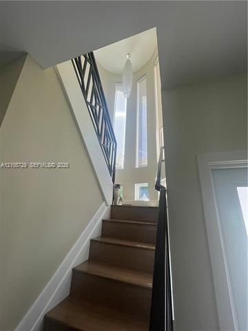 Staircase featuring wood-finish treads, geometric metal railing, vertical windows, and a suspended pendant fixture