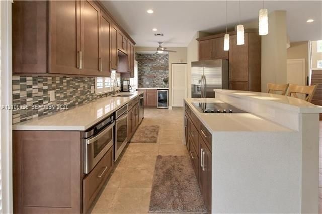 Kitchen featuring stained wood cabinetry, quartz countertops, a multi-tonal tile backsplash, stainless steel appliances, and tile flooring