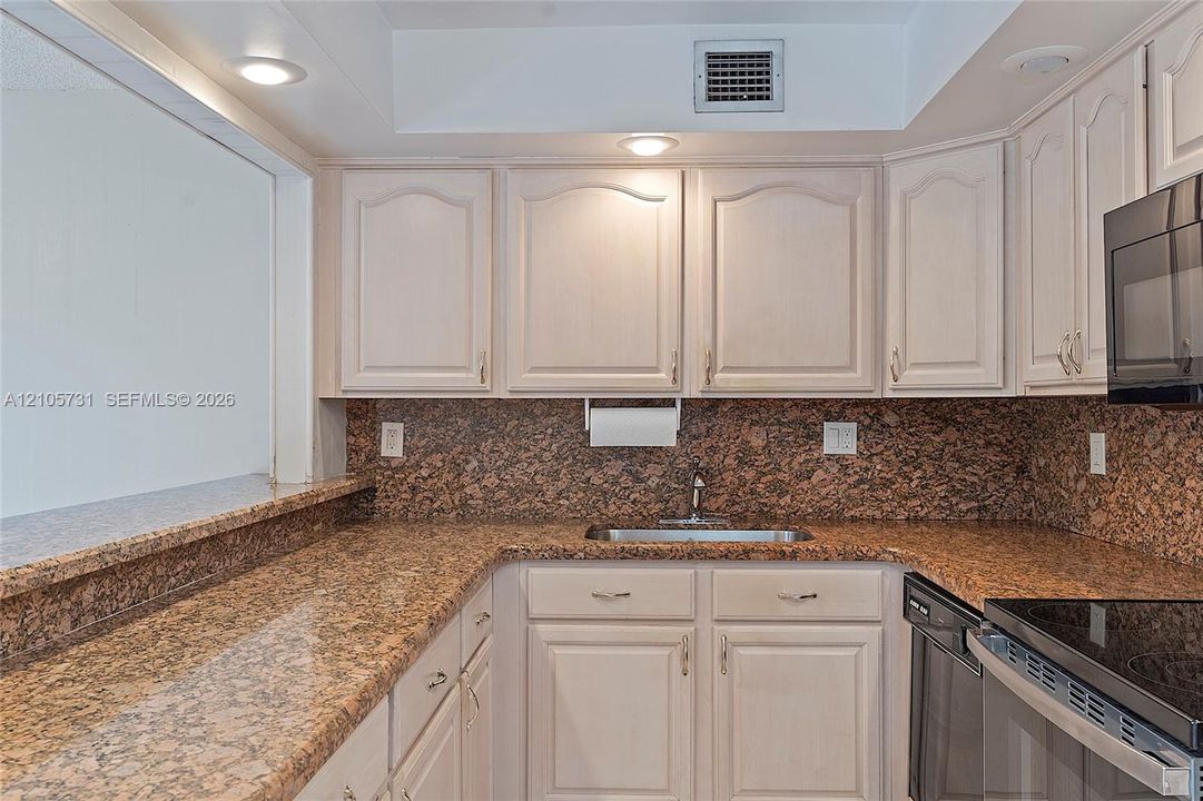 Kitchen featuring stone countertops, stone tile backsplash, light-finish cabinetry, built-in black microwave, and recessed lighting