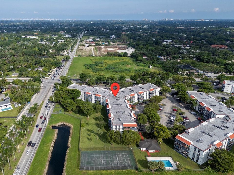 Aerial view featuring multi-story residential buildings, an outdoor swimming pool, and a fenced tennis court