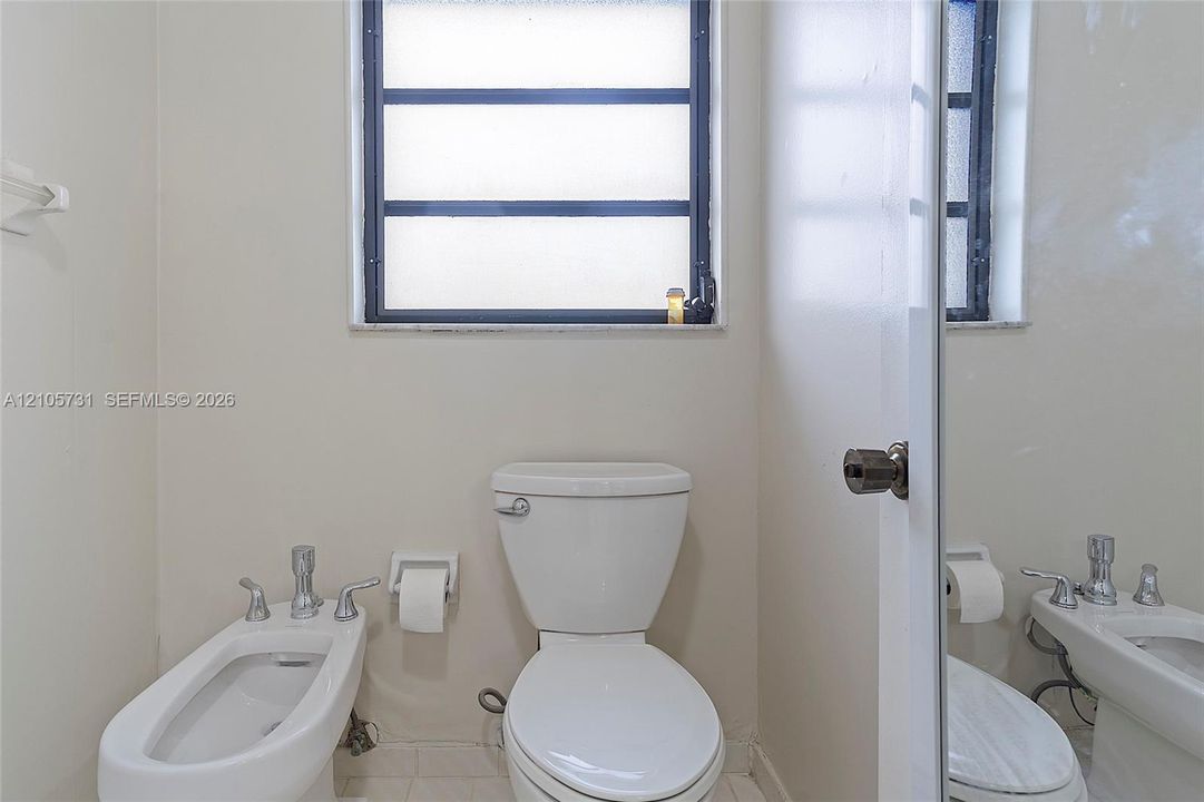 White ceramic toilet, bidet with chrome faucet hardware, and horizontal-pane window with dark frame