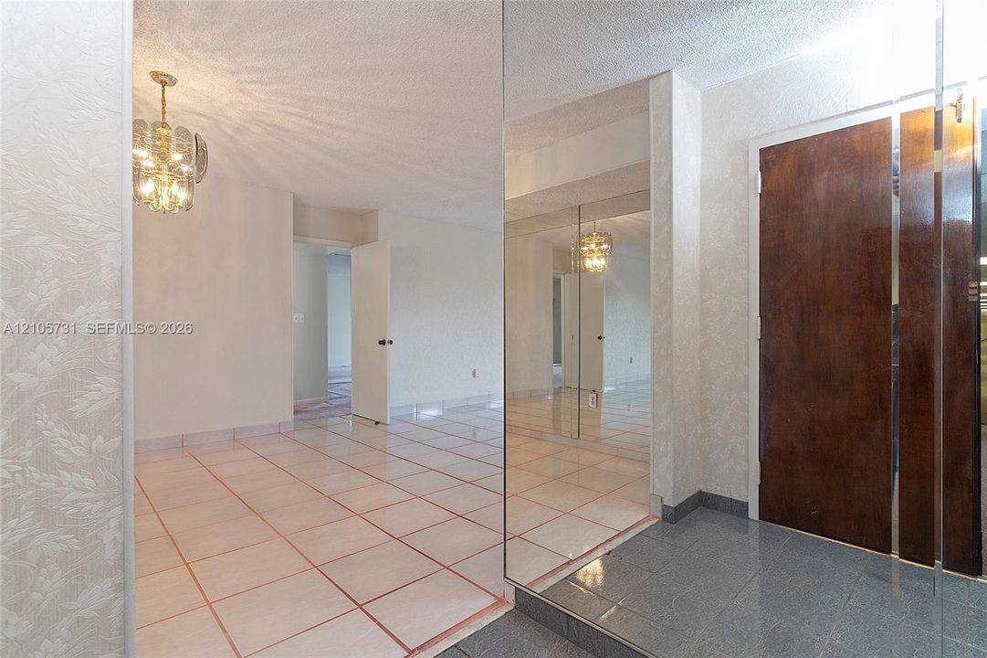 Entryway featuring a stone-tile floor, floor-to-ceiling mirrored wall panels, decorative multi-tiered pendant lighting, and a solid wood door with brushed metal trim