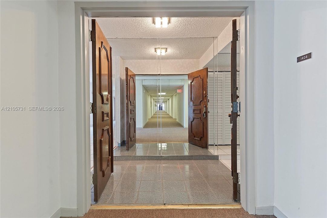 Entryway featuring double solid-wood doors with decorative panels, polished stone-finish floor tiling, and integrated wall-to-wall mirror paneling