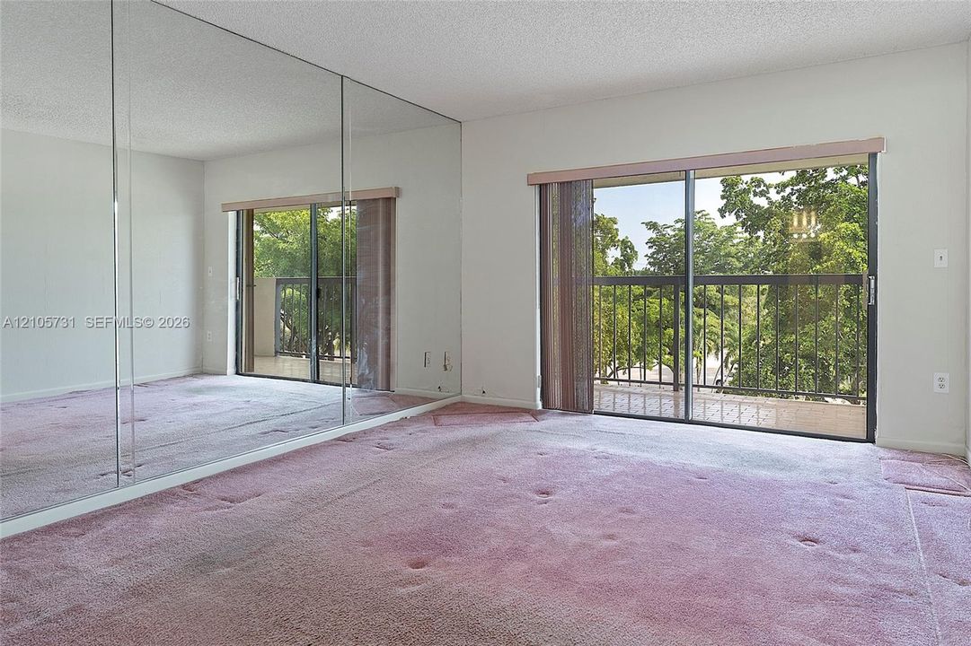 Full-wall mirrored closet doors, sliding glass door with balcony access, and exterior metal railings