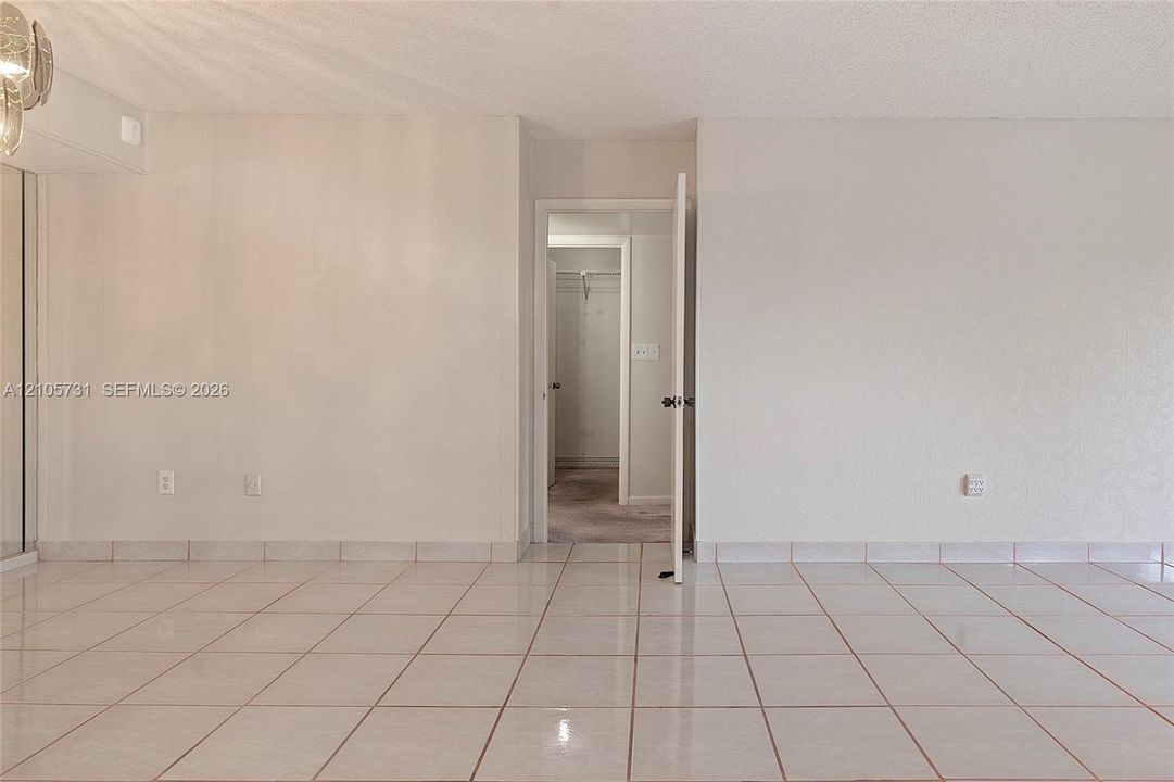 Neutral ceramic tile flooring and interior swing door leading to a walk-in closet with built-in shelving