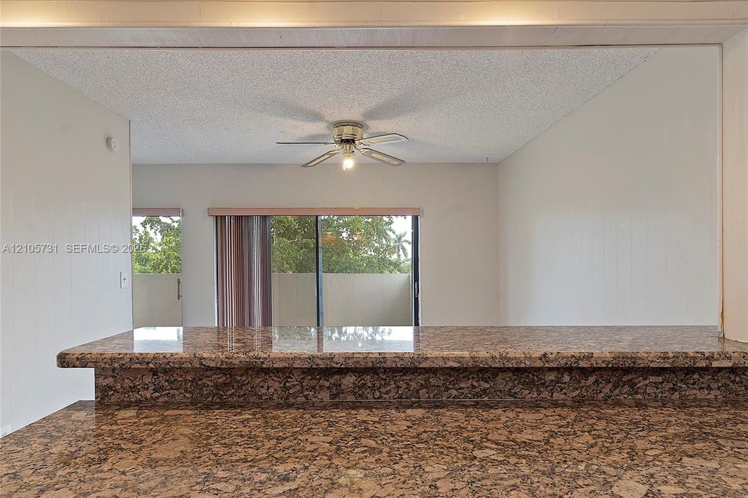 Stone-surfaced breakfast bar with an extended overhang, textured ceiling finish, and ceiling-mounted fan
