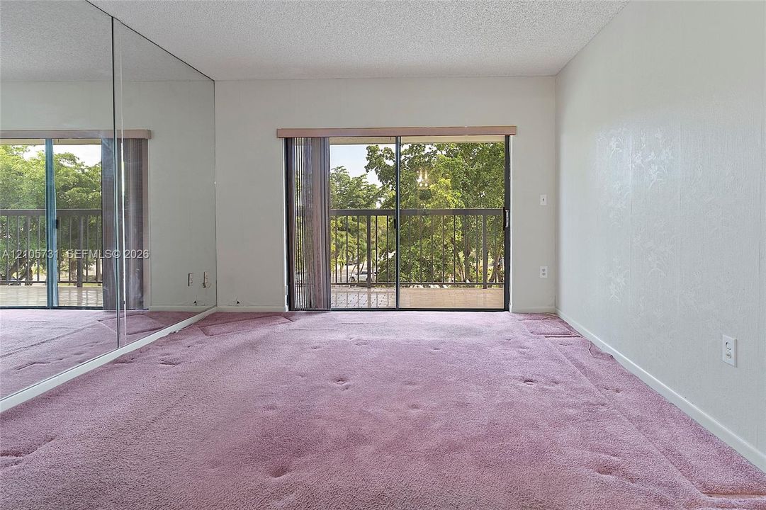 Room featuring a wall of floor-to-ceiling mirror panels, carpeted flooring, and a sliding glass door providing external access to a balcony with metal railings