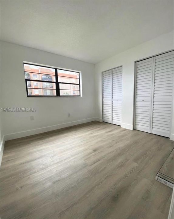 Wood-finish flooring, two sets of white louvered-style closet doors, and a large horizontal window with a black frame