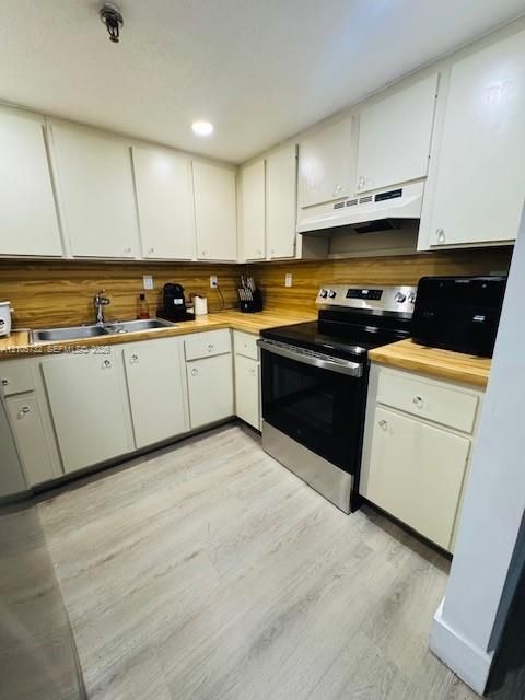 Kitchen featuring flat-panel cabinetry, wood-finish countertops, stainless steel range with overhead vent hood, dual-basin stainless steel sink, and light-toned wood-finish flooring
