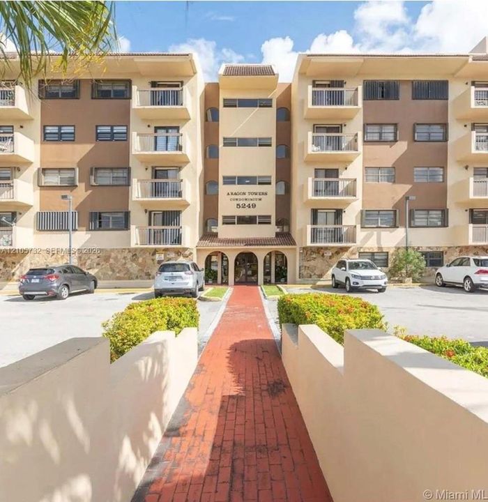 Multi-story condominium exterior featuring a stone-clad facade, private balconies, an arched entryway, and a paved brick walkway