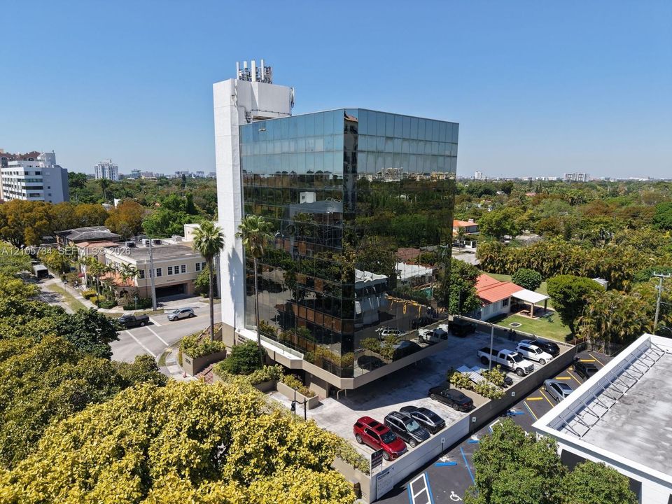 Multi-story professional building featuring a mirrored glass curtain wall, concrete structural tower, and an integrated surface parking lot