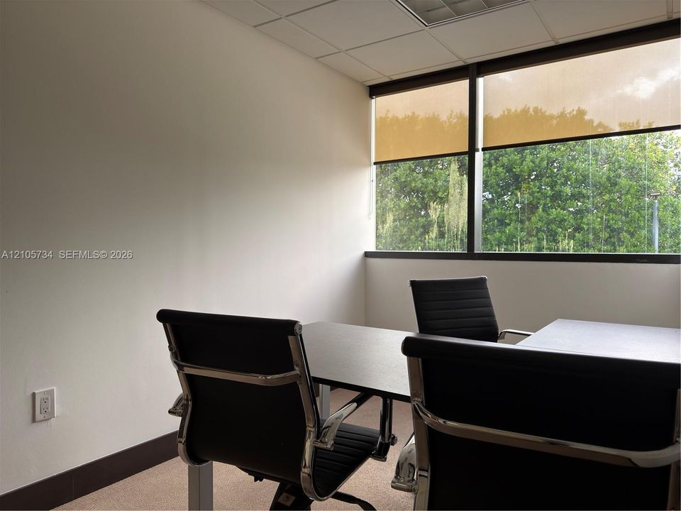 Corner office featuring expansive horizontal windows, neutral wall finishes, drop ceiling tiles, and neutral carpeting