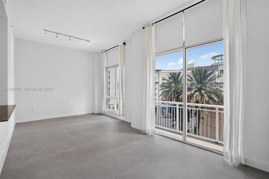 Floor-to-ceiling windows, large-format tile flooring, industrial-style track lighting, and a private balcony with metal railing