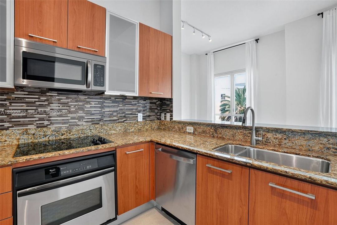 Kitchen featuring wood-finish cabinetry, natural stone countertops, a mosaic tile backsplash, stainless steel appliances, and a double-basin undermount sink with a gooseneck faucet