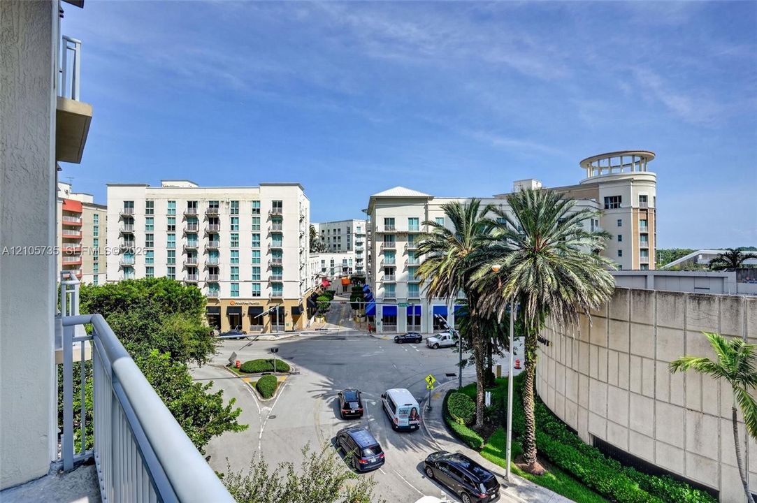 Elevated balcony featuring a metal railing with a clear sightline of the surrounding urban streetscape and palm trees