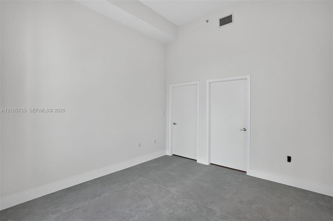 High-ceiling interior featuring matte neutral wall finishes, large-format tile flooring, and two flush-panel interior doors with brushed metallic hardware