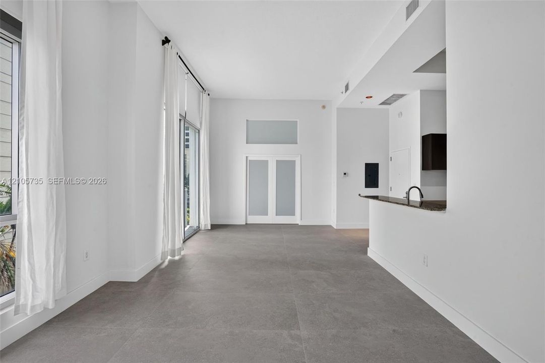 High-ceiling interior featuring full-height windows, large-format tile flooring, double doors with frosted glass panels, and a built-in counter with a sink