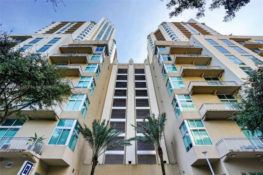 High-rise residential exterior featuring tiered concrete balconies, multi-story glass pane windows, and a central architectural column with integrated horizontal paneling