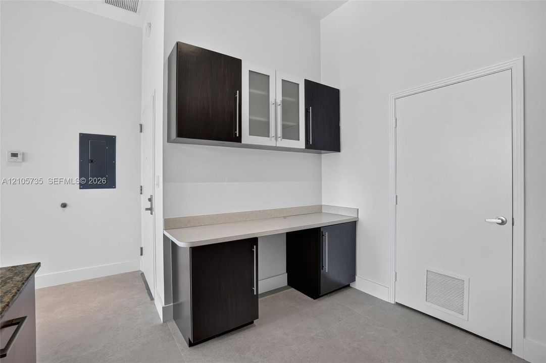 Built-in cabinetry featuring dark finish lower cupboards, contrasting upper cabinets with glass-front detailing, and stone-finish countertop