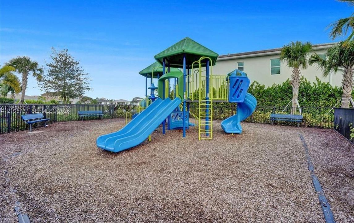 Recreational area featuring a multi-level playground structure, slide components, metal benches, and organic ground cover