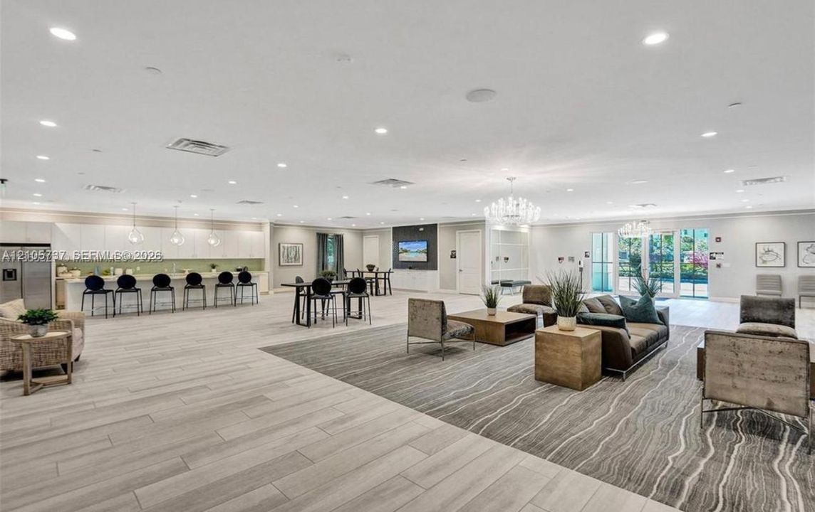 Open-concept interior featuring light wood-finish flooring, recessed lighting, expansive built-in cabinetry with integrated bar seating, and multi-tier decorative chandeliers