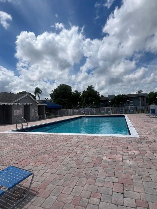 Rectangular swimming pool featuring a brick paver deck, metal safety fencing, and attached poolside utility structure