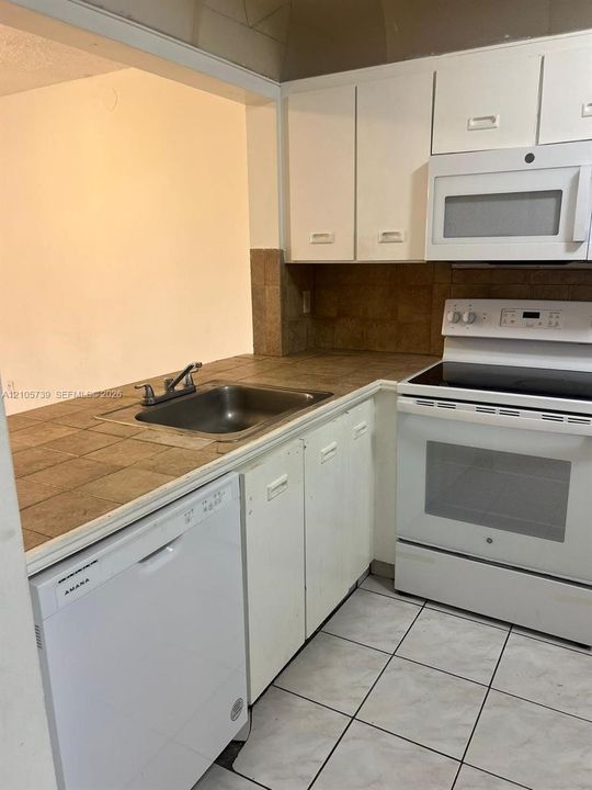 Kitchen featuring white cabinetry, tile countertops, tile flooring, an over-the-range microwave, and a stainless steel sink