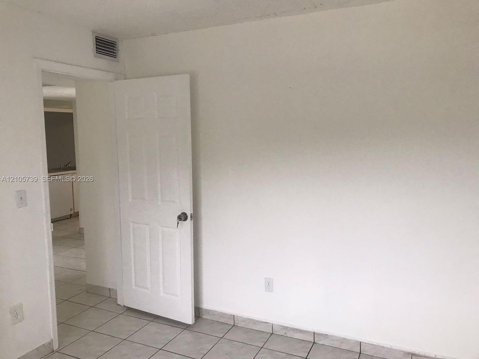 Neutral interior featuring ceramic tile flooring, a six-panel door with metal hardware, and white-painted walls