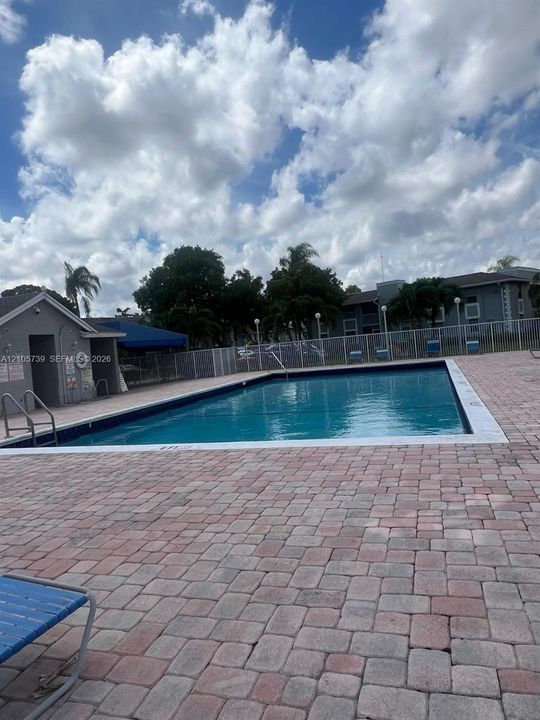 Rectangular swimming pool featuring a brick paver deck, metal safety fencing, and built-in access ladders