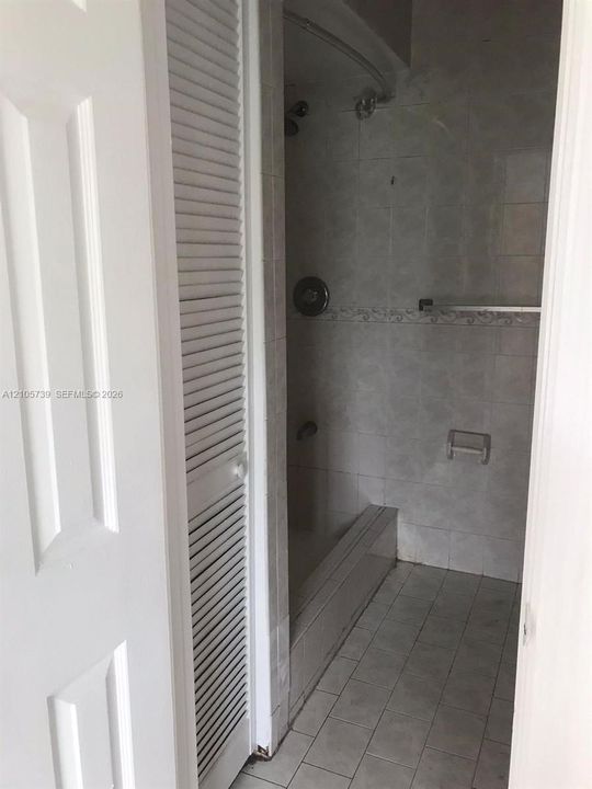 Shower area featuring floor-to-ceiling tile, an integrated tub surround, a curved shower rod, and louvered bi-fold doors
