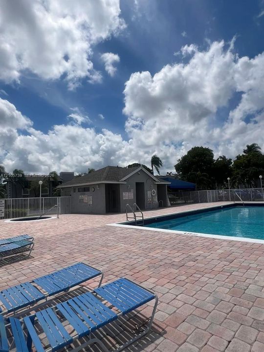 Outdoor swimming pool and spa area featuring brick paver decking and a covered utility structure enclosed by metal fencing