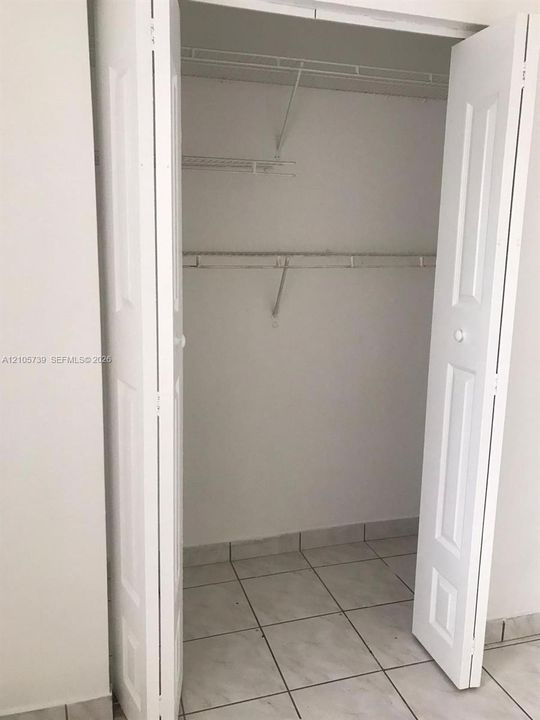 Reach-in closet featuring white paneled bifold doors, wire shelving, and neutral tile flooring