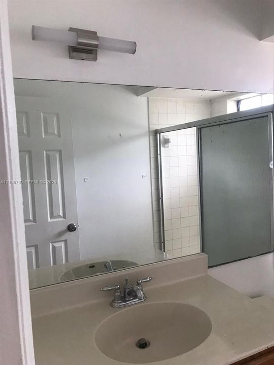 Bathroom vanity featuring a solid-surface countertop with an integrated basin, dual-handle faucet, full-width mirror, and wall-mounted light fixture, complemented by a shower enclosure with sliding doors