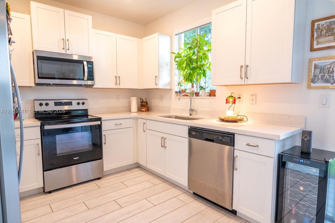 Kitchen featuring white shaker-style cabinetry, stainless steel appliances, light-toned solid surface countertops, a stainless steel undermount sink, and wood-finish tile flooring