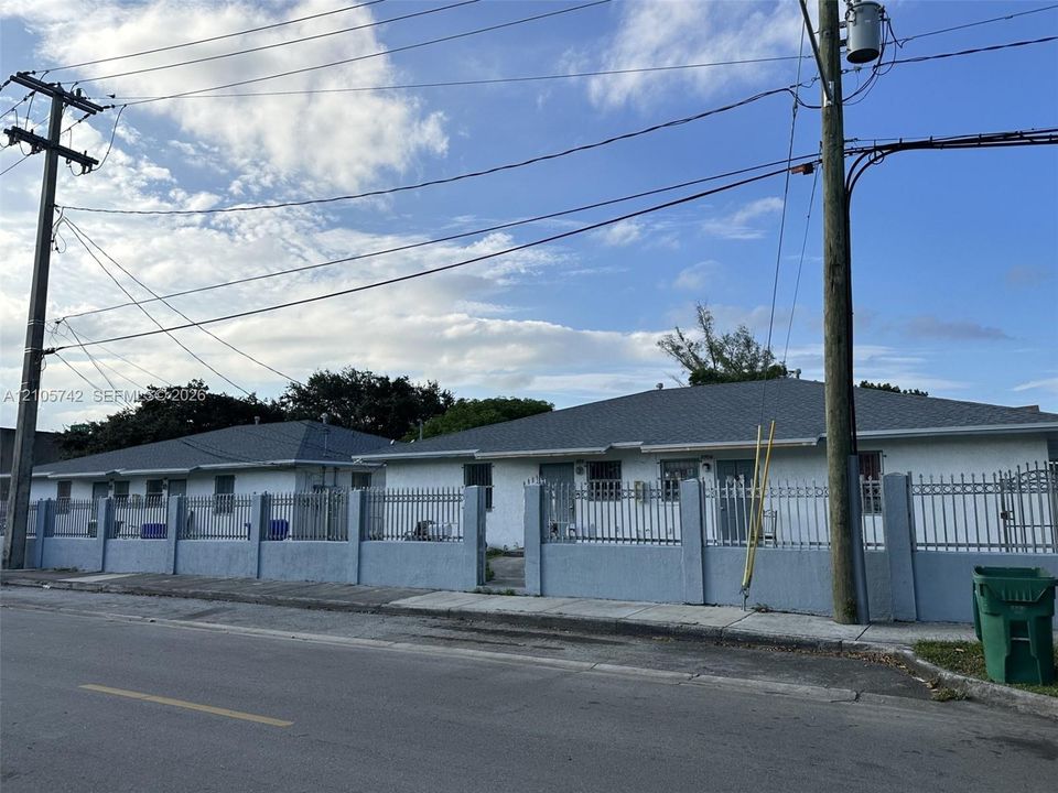 Single-story structure featuring a concrete exterior, multi-hipped shingle roof, and a perimeter concrete wall with integrated metal fencing