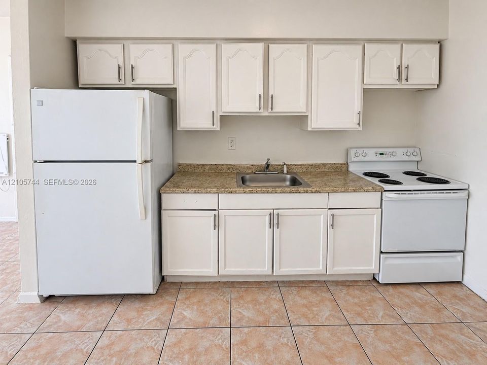 Kitchenette featuring white cabinetry, stone-finish countertops, stainless steel sink, tile flooring, and integrated white appliances