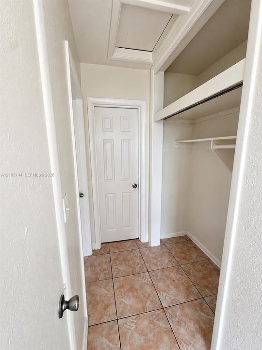 Storage area featuring ceramic tile flooring, a six-panel interior door, and built-in shelving with a clothes rod