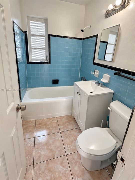 Bathroom featuring blue square-tile wall surround with black accent trim, white vanity with integrated sink, porcelain bathtub, and neutral-toned tiled flooring