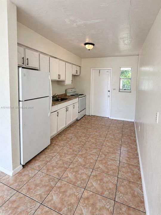 Kitchen featuring white shaker-style cabinetry, speckled stone-surface countertops, tile flooring, and integrated white appliances