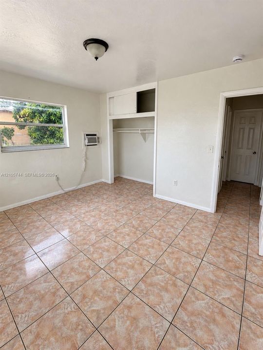 Room featuring neutral-toned wall-to-wall ceramic tile flooring, a built-in closet with overhead storage cabinet, a flush-mount ceiling light fixture, and a window providing natural light