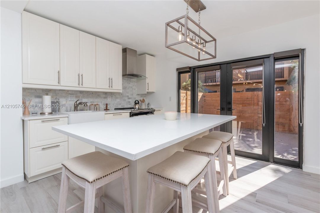 Kitchen featuring custom cabinetry, a central island with a solid surface countertop, a tiled backsplash, and framed glass patio doors