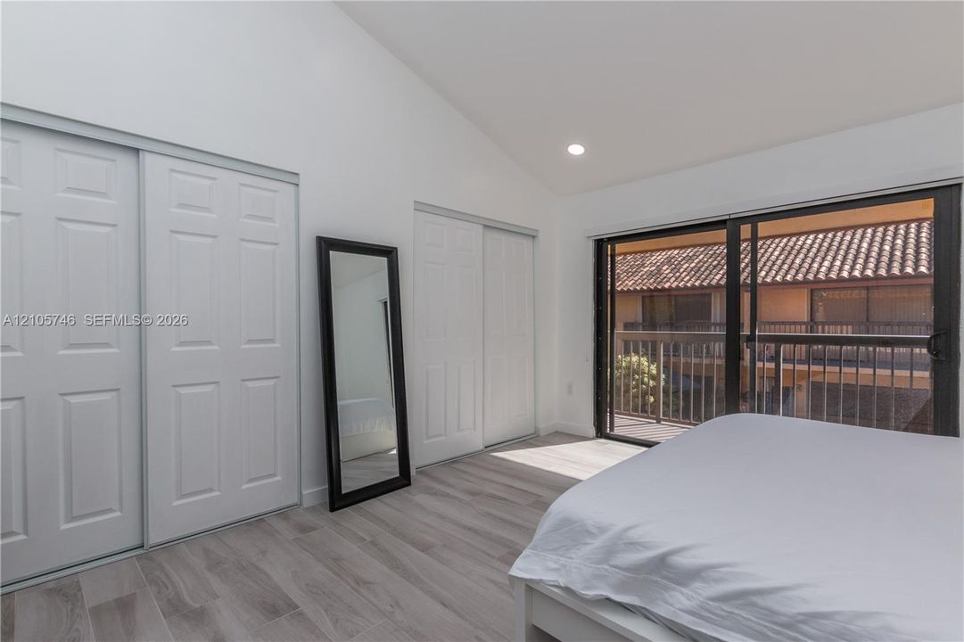 Vaulted ceilings, wood-finish tile flooring, dual closets with raised-panel sliding doors, and a sliding glass door providing access to a balcony