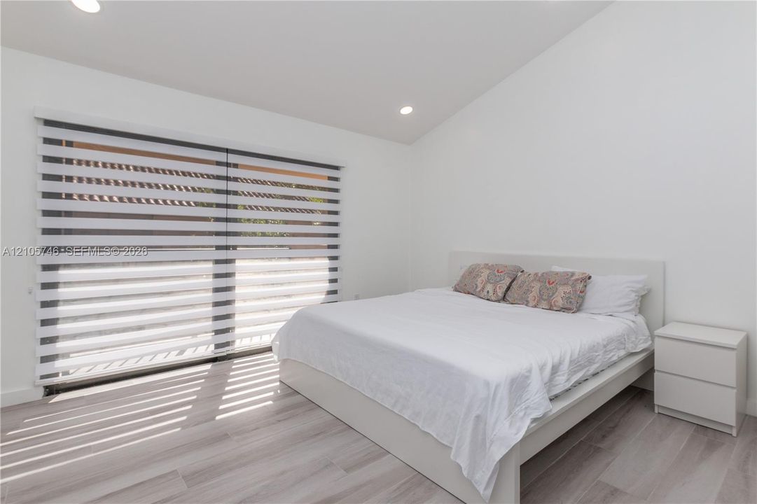 Vaulted ceiling, wood-finish flooring, and expansive sliding glass doors featuring dual-layered roller shades