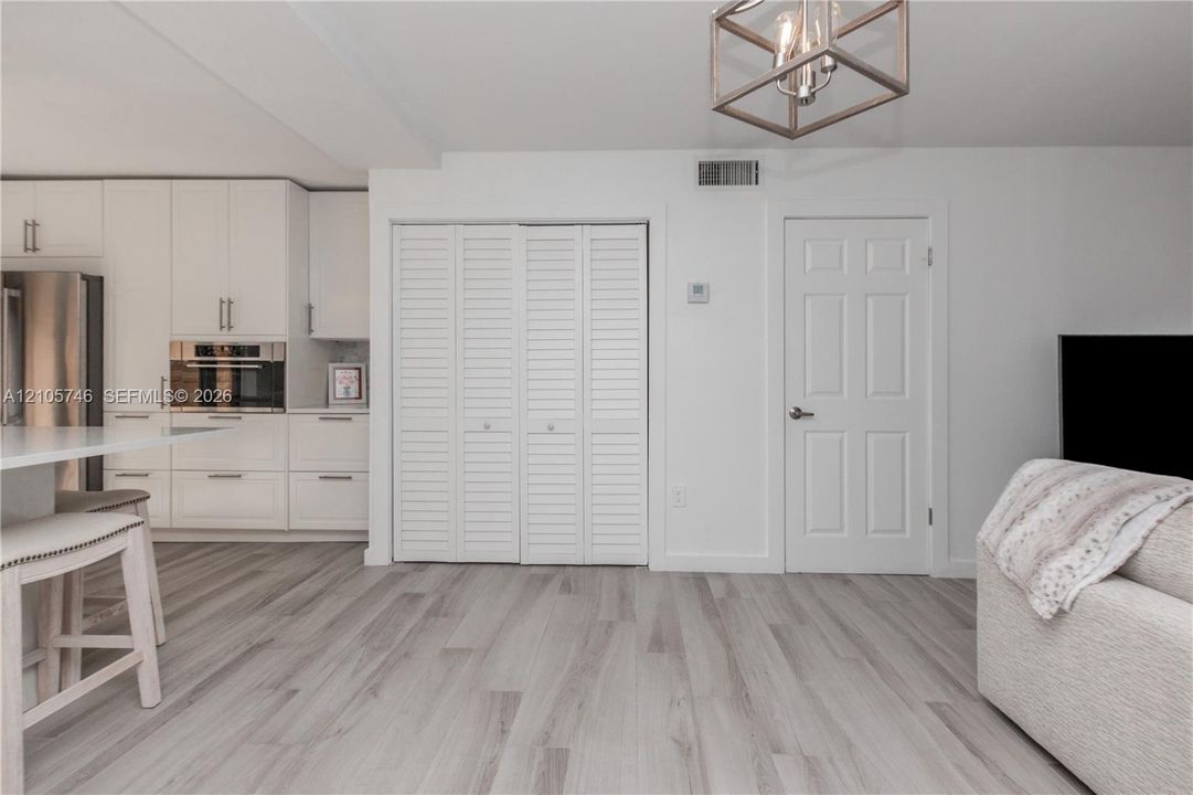 Modern kitchen featuring white flat-panel cabinetry, stainless steel built-in oven, wood-finish flooring, white louvered closet doors, and a geometric pendant light fixture