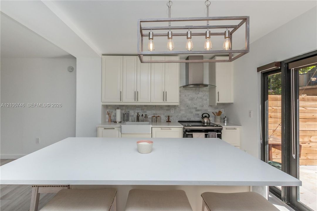 Kitchen featuring solid-surface countertops, a farmhouse-style apron sink, custom cabinetry, a stainless steel chimney-style range hood, and a rectangular metal-frame chandelier