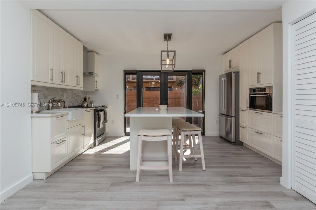Kitchen featuring white cabinetry, center island with stone countertop, apron-front sink, stainless steel appliances, and wood-finish flooring