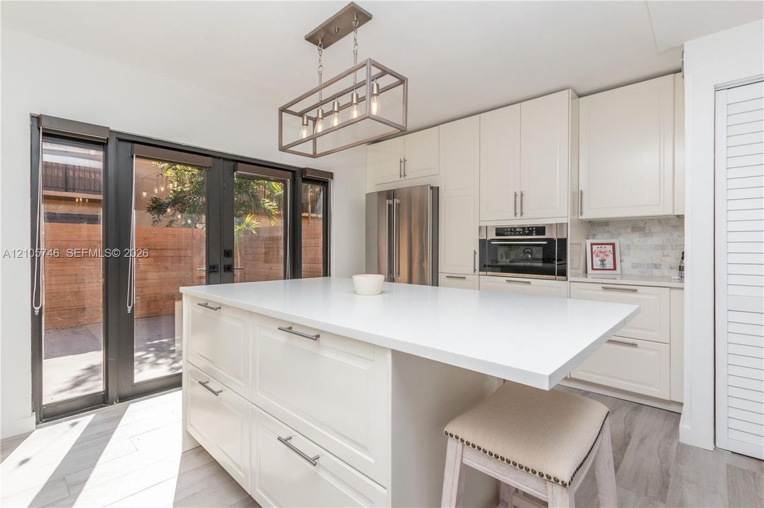 Kitchen featuring a central island with a solid surface countertop, white shaker-style cabinetry, stainless steel appliances, a linear four-light pendant fixture, and wood-finish flooring